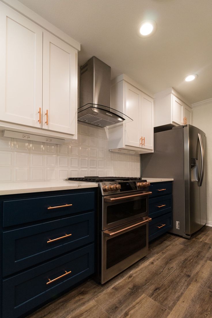 a kitchen with white cabinets and dark blue drawers, stainless steel appliances and wood flooring