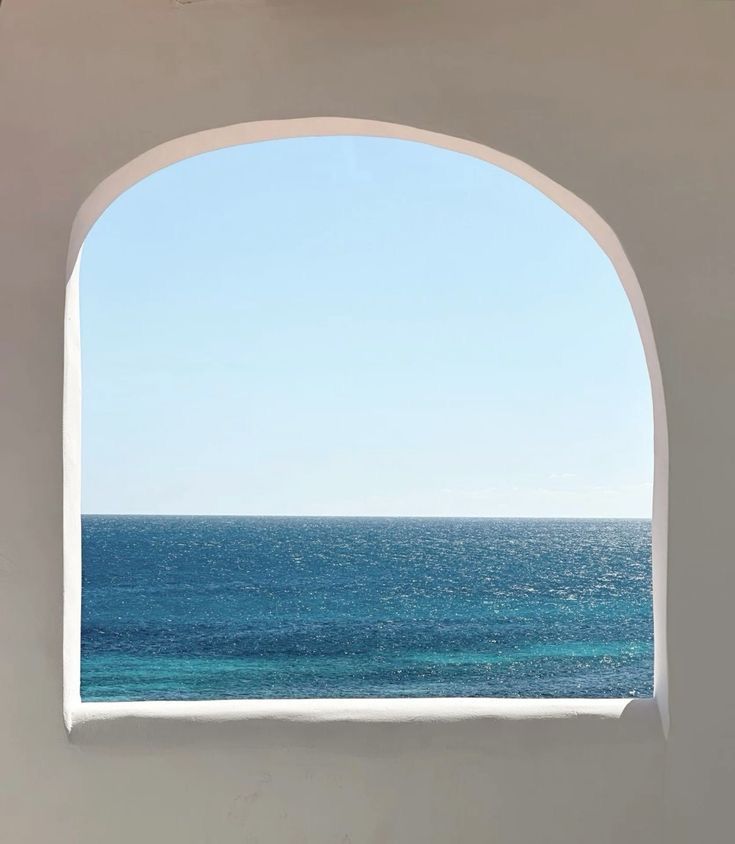 an open window with the view of the ocean and blue sky from inside a building