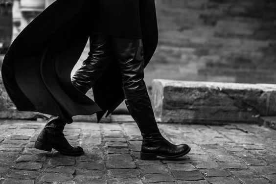 black and white photograph of person walking on cobblestone street with coat over head