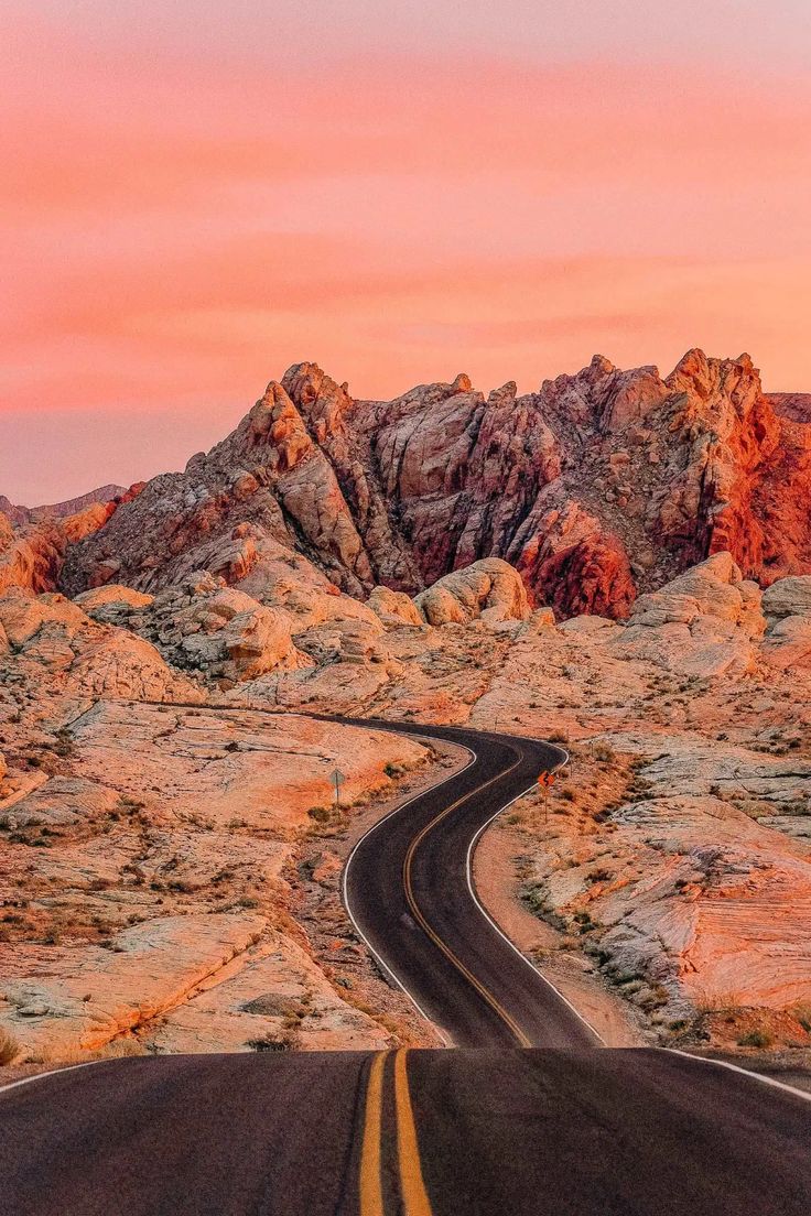 an empty road in the desert with mountains in the background at sunset or sunrise time