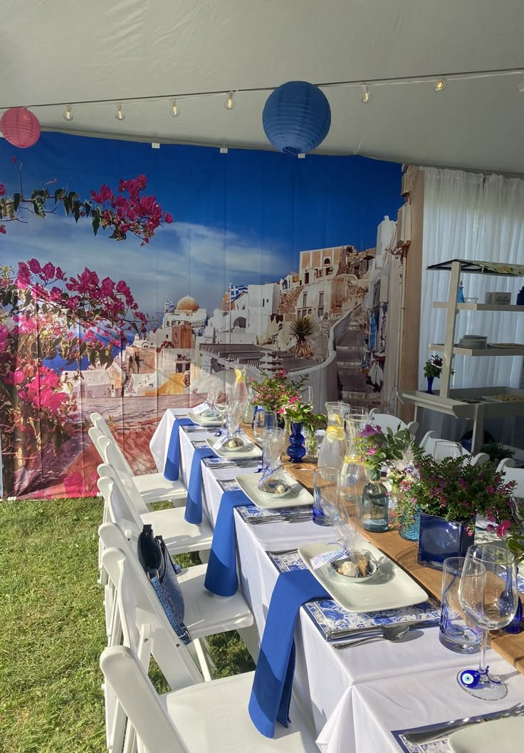 a long table set up with blue and white linens for an outdoor dinner party