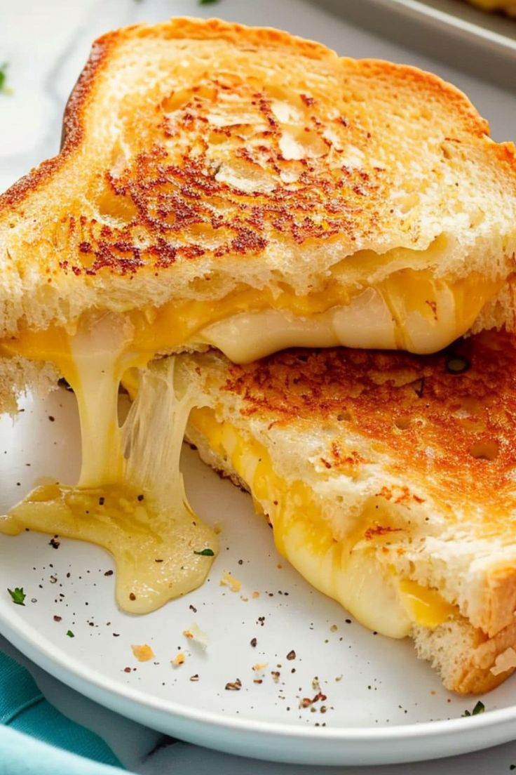 a grilled cheese sandwich on a white plate with melted cheese and mustard drizzled over it