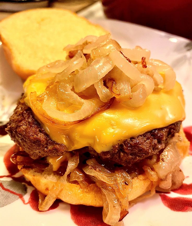 a cheeseburger with onions on a plate next to a slice of toasted bread