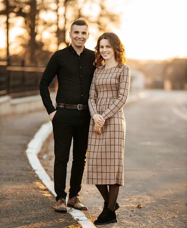 a man and woman standing next to each other on the street in front of trees