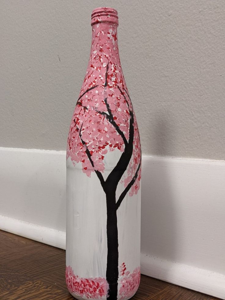 a painted bottle sitting on top of a wooden floor next to a wall with a tree in it