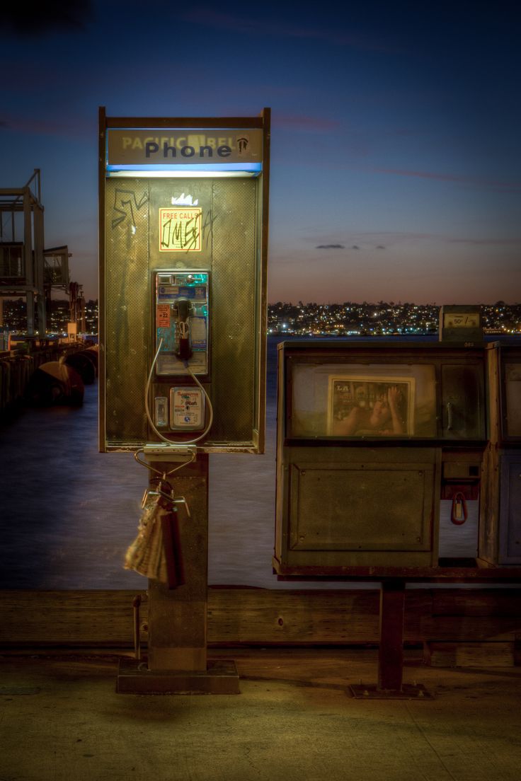 an old fashioned pay phone sitting on top of a wooden bench next to the ocean