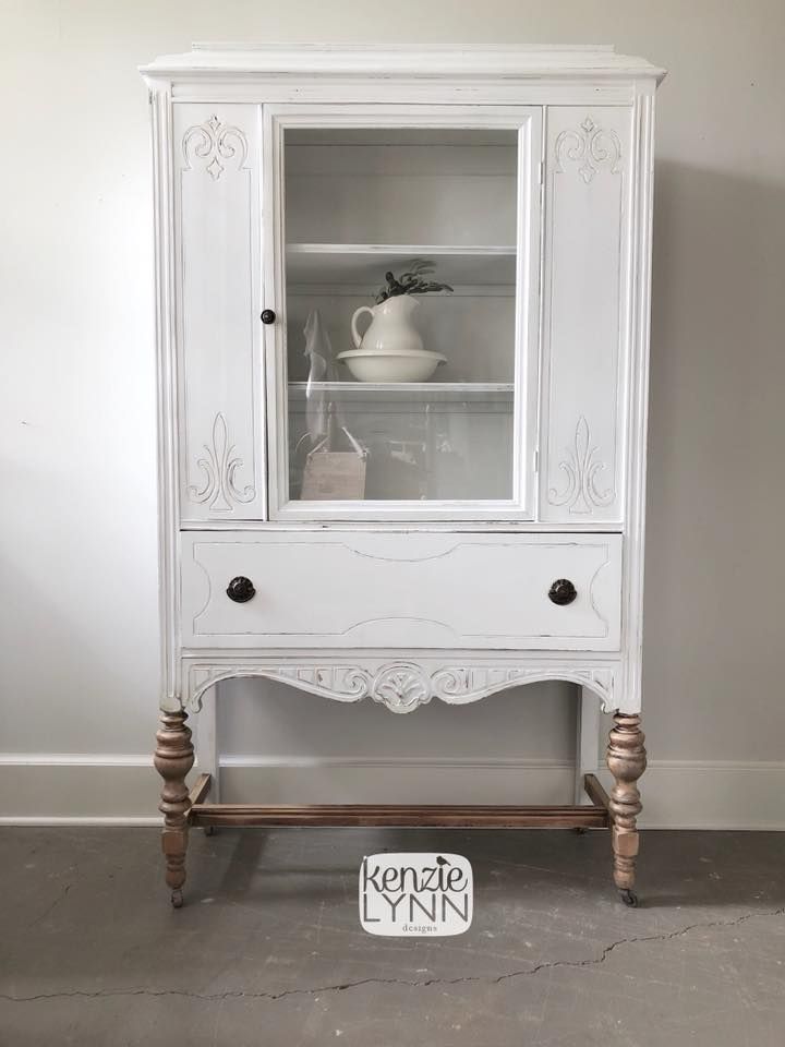 a white china cabinet with glass doors and drawers on the bottom, in front of a gray wall