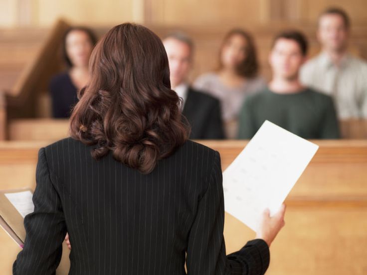 a woman in a black suit is holding a piece of paper and looking at other people