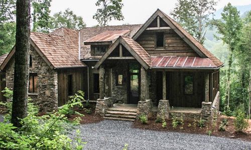 a rustic cabin in the woods with stone and wood accents on the front door, windows, and porch