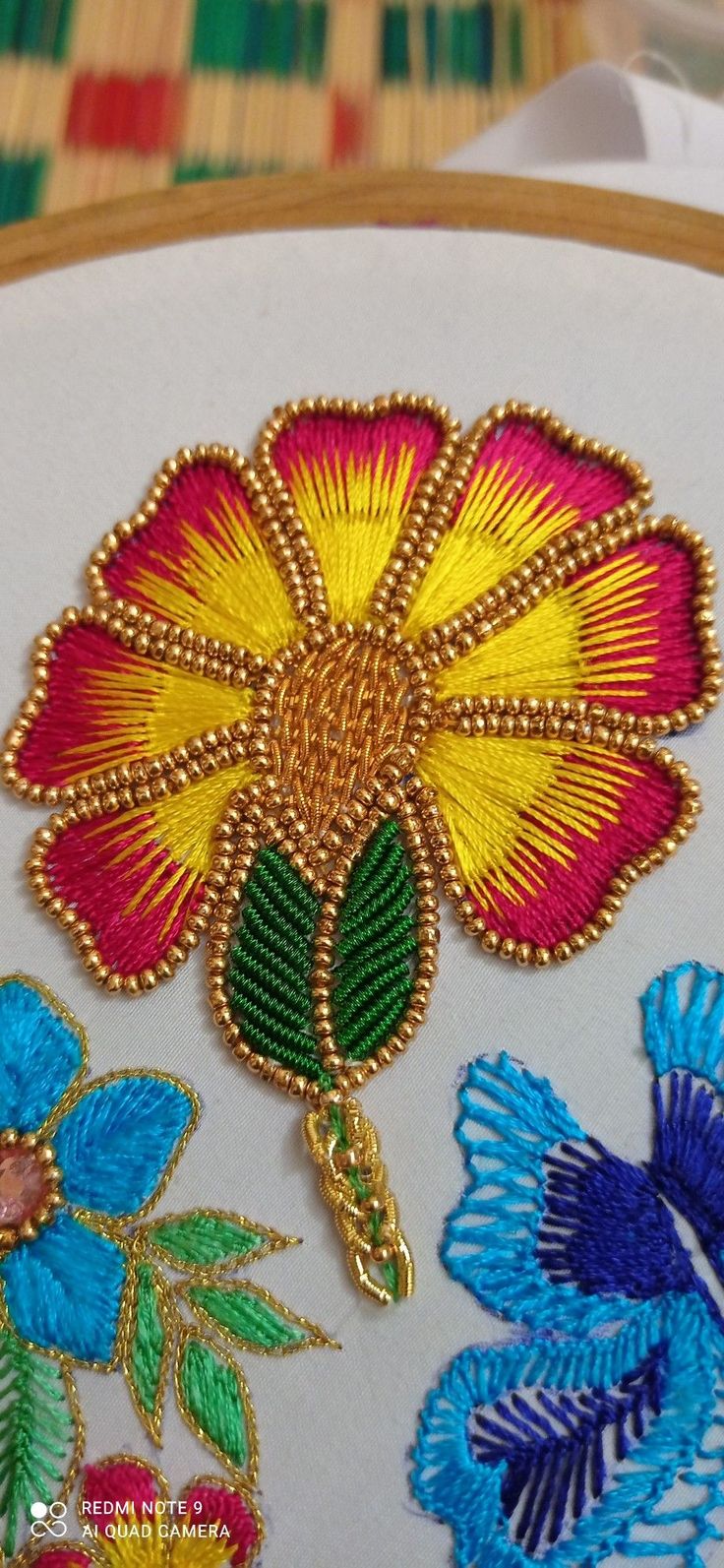 a close up of some embroidery on a piece of cloth with flowers in the background