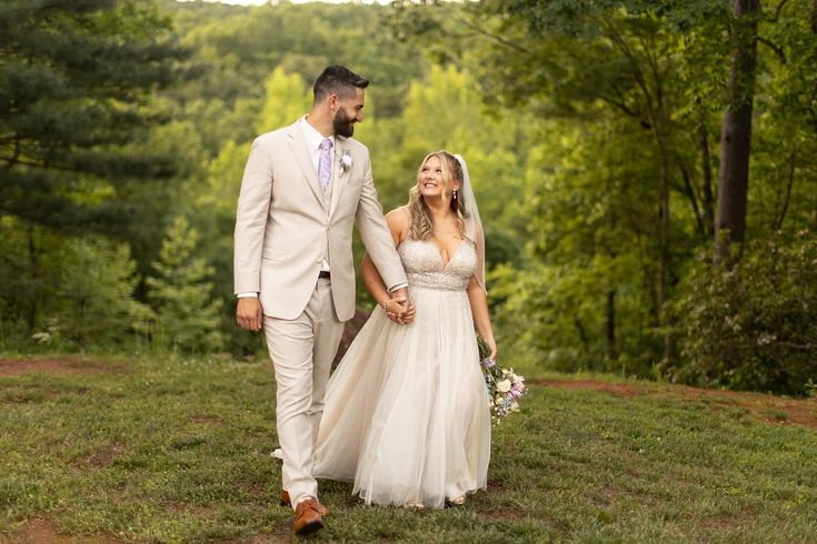 a bride and groom are walking through the woods in their wedding attire, holding hands