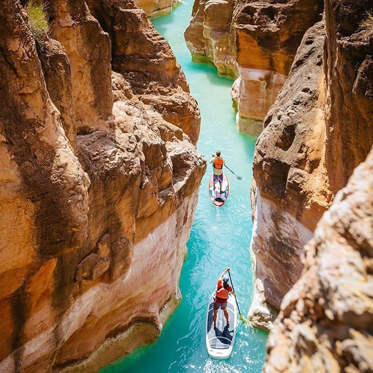 two people in small boats on a river surrounded by rocky cliffs and canyons with blue water