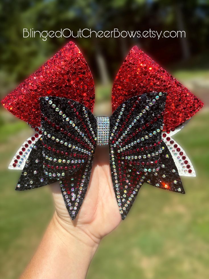 a hand holding a red and black bow with lots of sequins on it