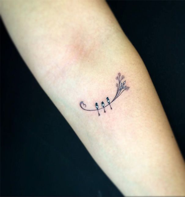 a small tattoo on the arm of a woman with three birds perched on an arrow