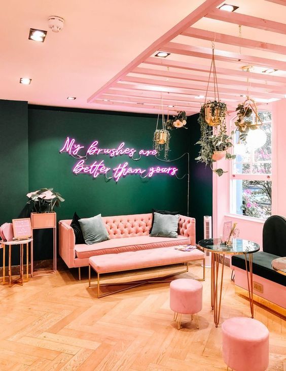 a living room with pink couches and chairs in front of a neon sign on the wall