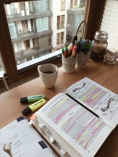 an open book sitting on top of a wooden table next to a cup and pen