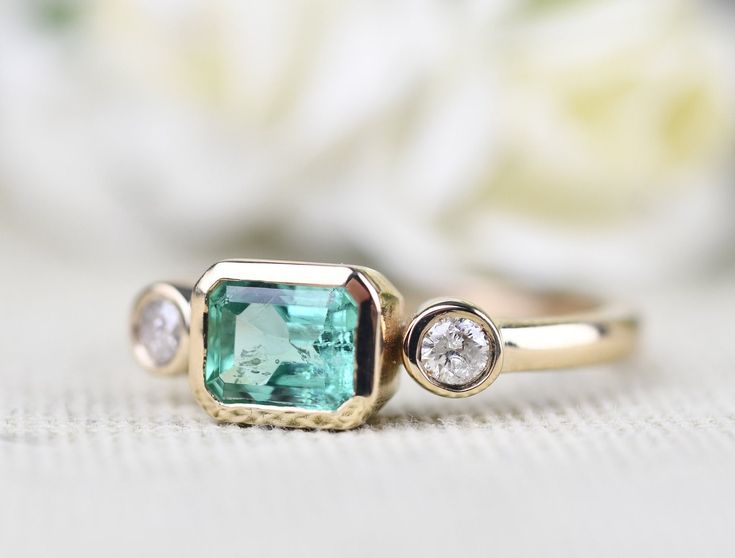 a close up of a ring with a green stone and two diamonds on the side