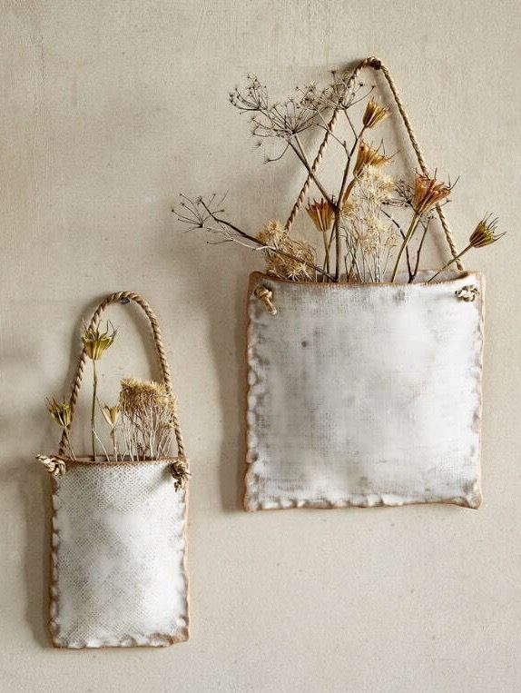 two white bags with dried flowers in them hanging on the wall next to each other