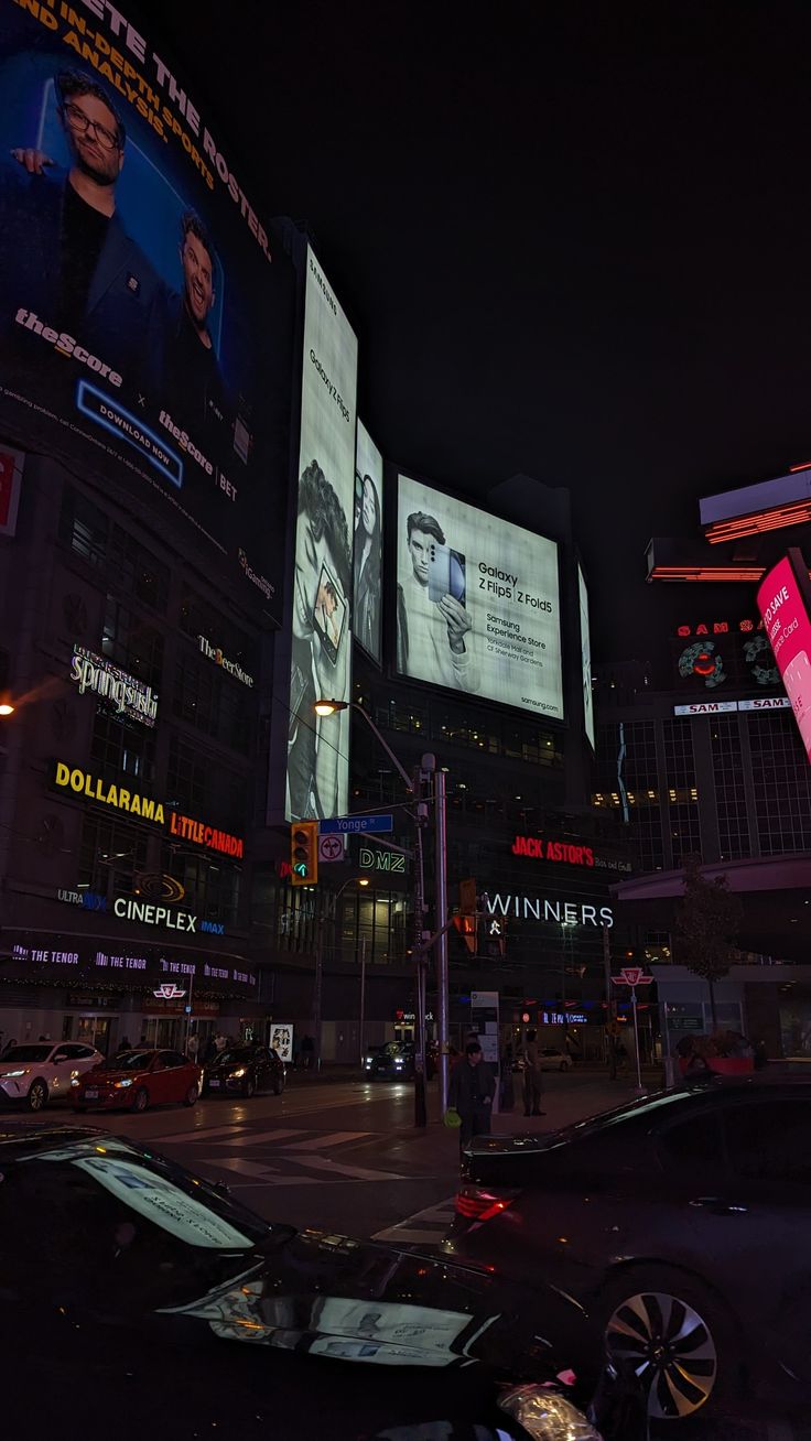 a city street filled with lots of traffic and tall buildings covered in billboards at night