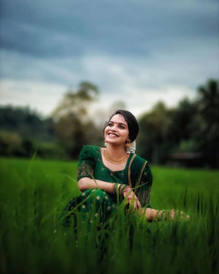 a woman sitting in the middle of a green field with her eyes closed and smiling