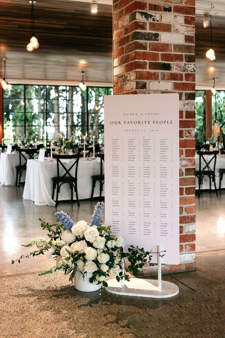 a table is set up with white flowers and greenery in front of a brick pillar