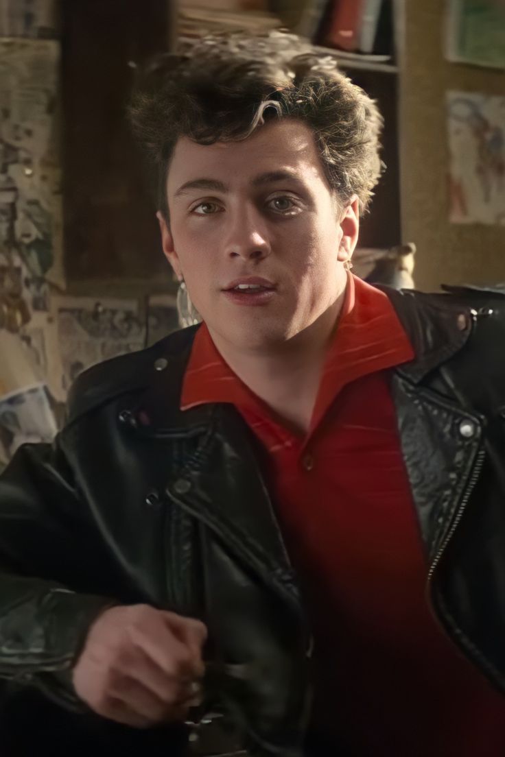 a young man wearing a black leather jacket and red shirt is looking at the camera