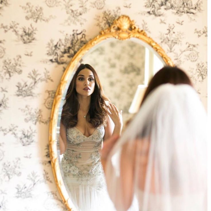 a woman in a wedding dress looking at herself in the mirror with her veil pulled back