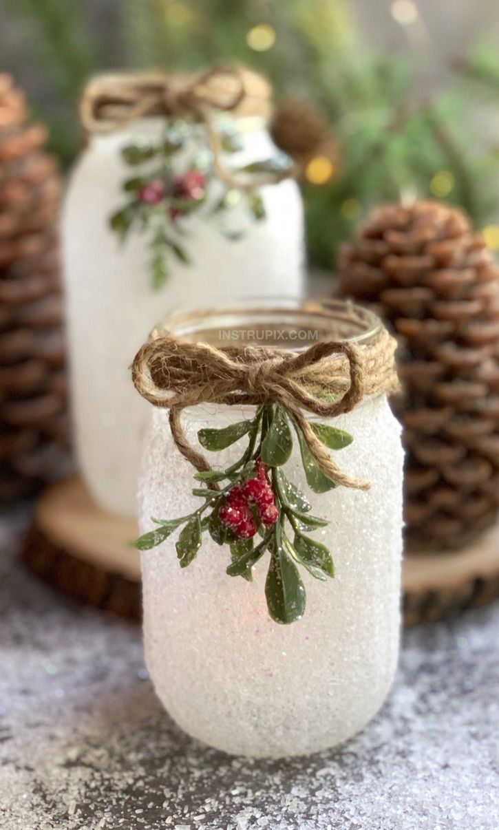 two mason jars decorated with holly and pine cones are sitting next to some pine cones