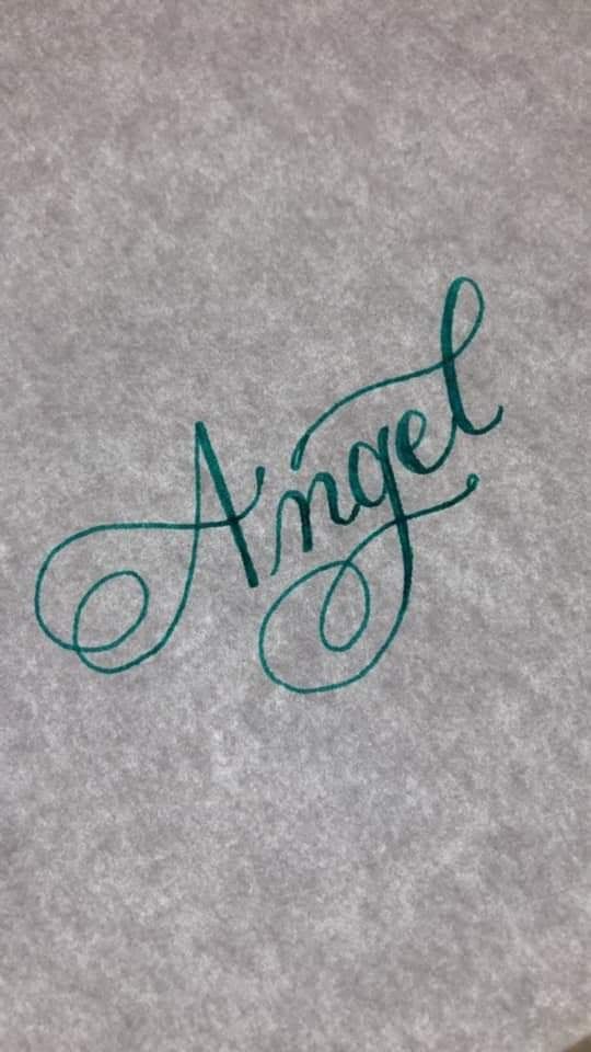 the word angel written in cursive writing on a gray surface with green ink