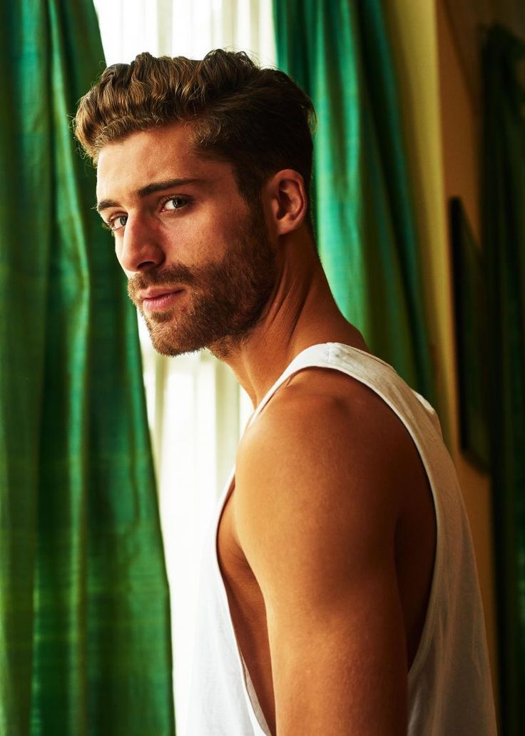 a man in white tank top standing next to green curtains