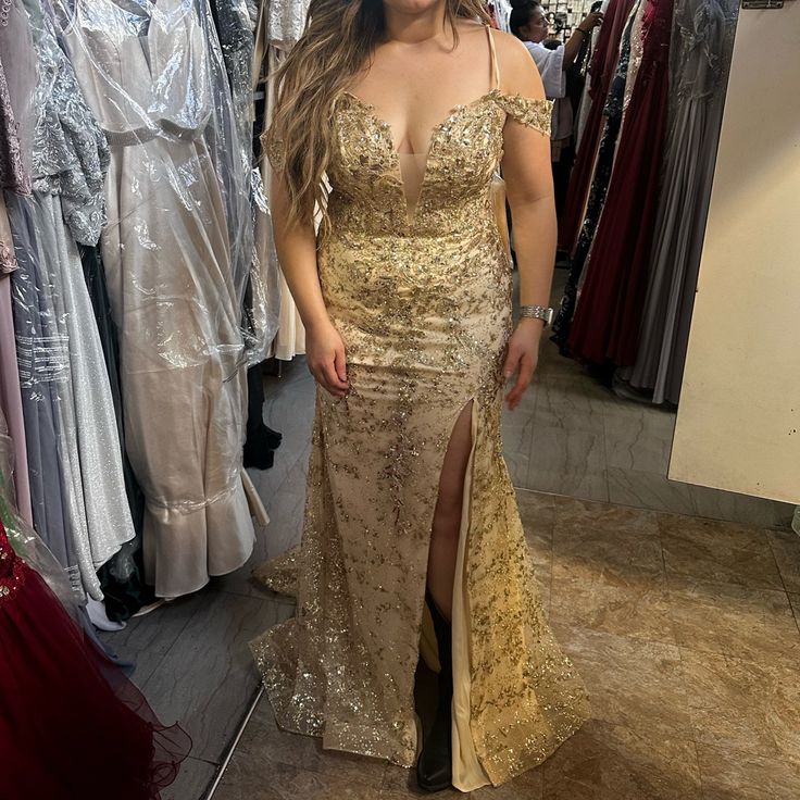 a woman standing in front of a mirror wearing a gold dress and posing for the camera