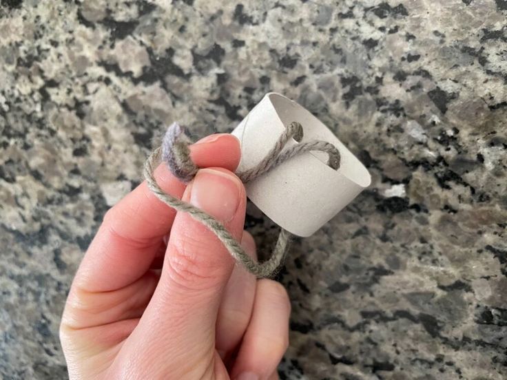 a hand holding a rope wrapped around a roll of toilet paper on top of a granite counter