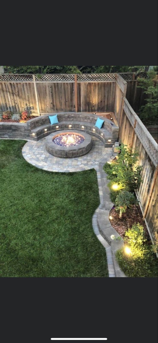 an outdoor fire pit in the middle of a yard with grass and lights around it