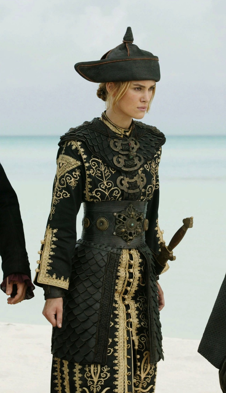 a woman in a black and gold outfit on the beach with two men walking behind her