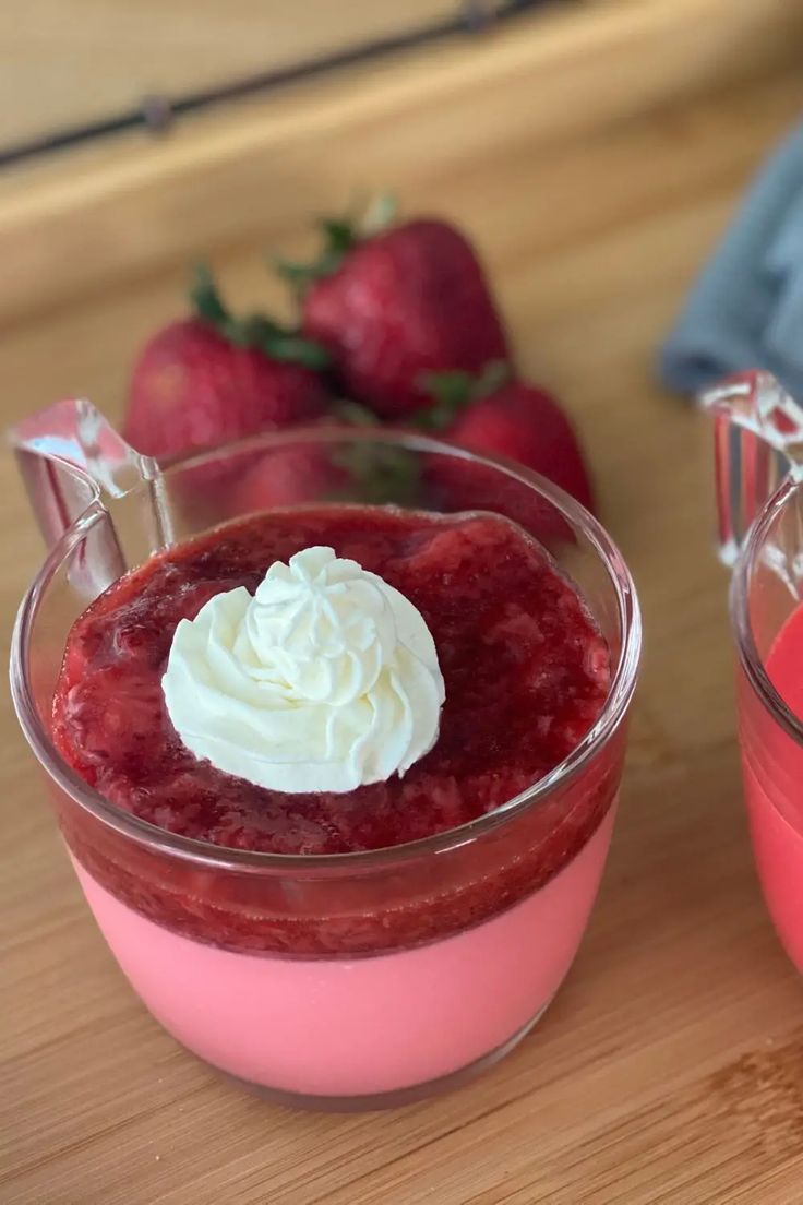 two desserts with strawberries and whipped cream on top sit on a table next to each other