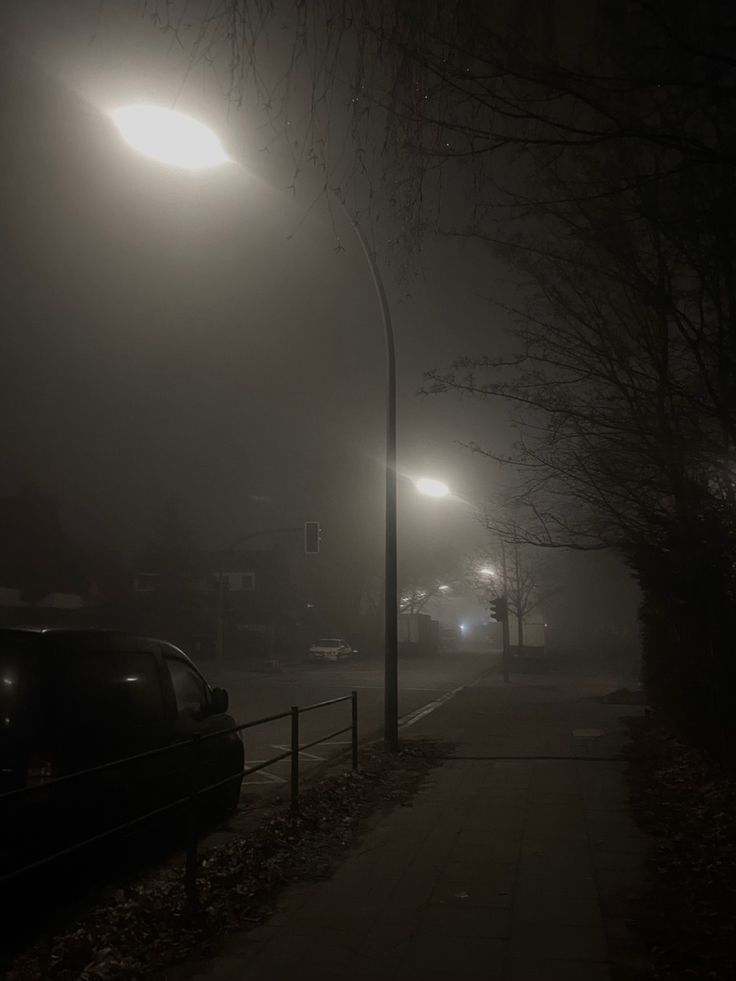 a foggy night with street lights and cars parked on the side of the road