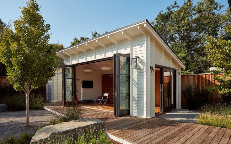 a small white house with wooden decking next to trees