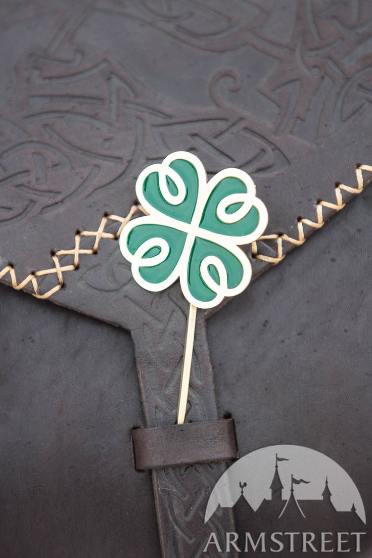 a green and white shamrock shaped pin on top of a black piece of paper with gold trim