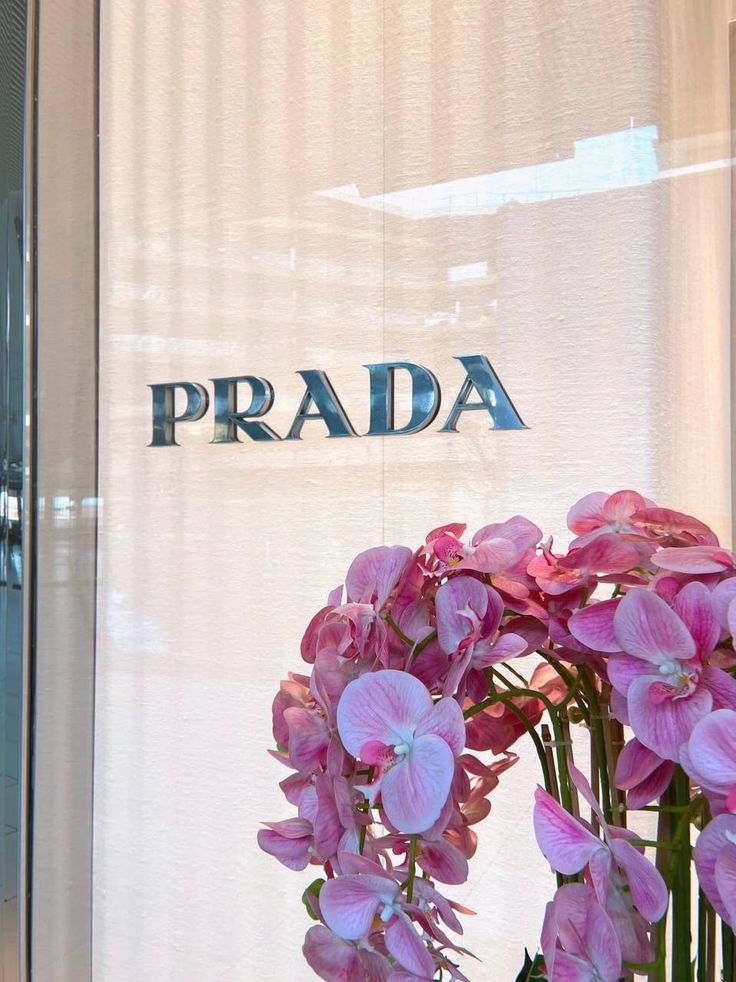 a vase with pink flowers in front of a prada storefront window display sign