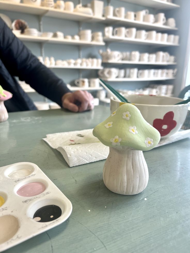 two people are sitting at a table in front of some cups and paintbrushes