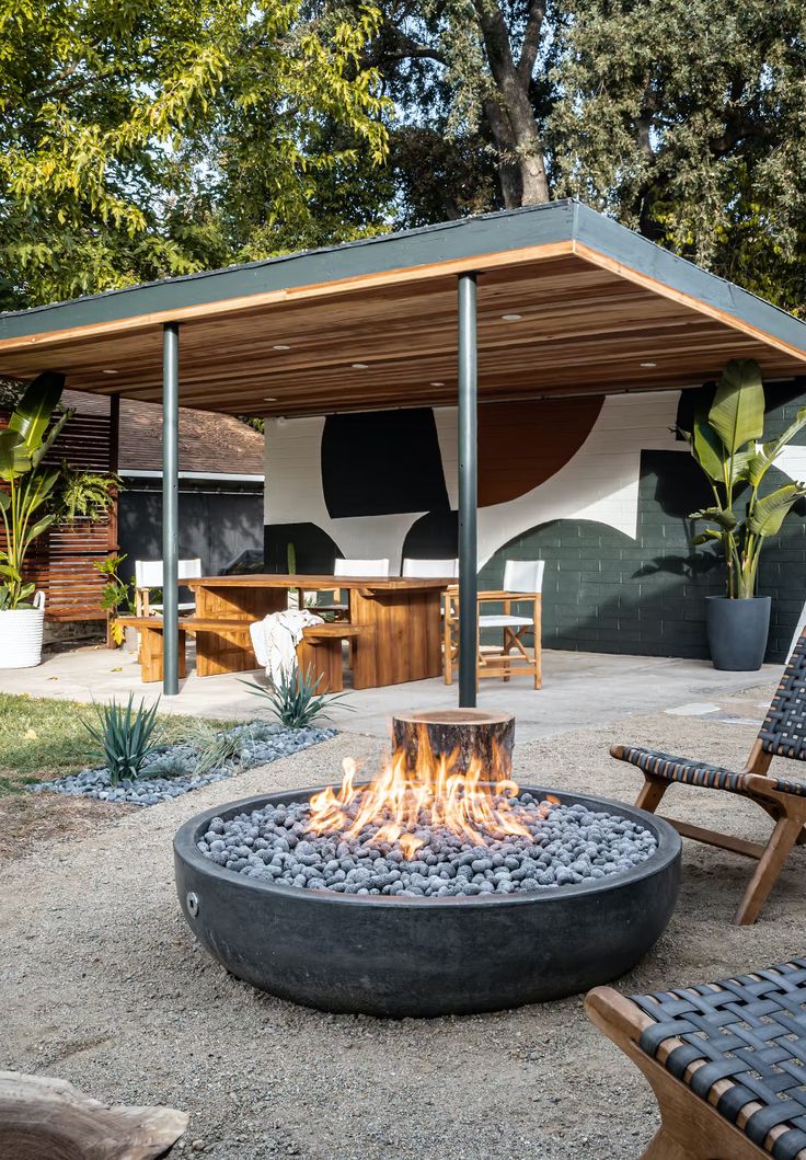 a fire pit sitting in the middle of a yard next to some chairs and tables