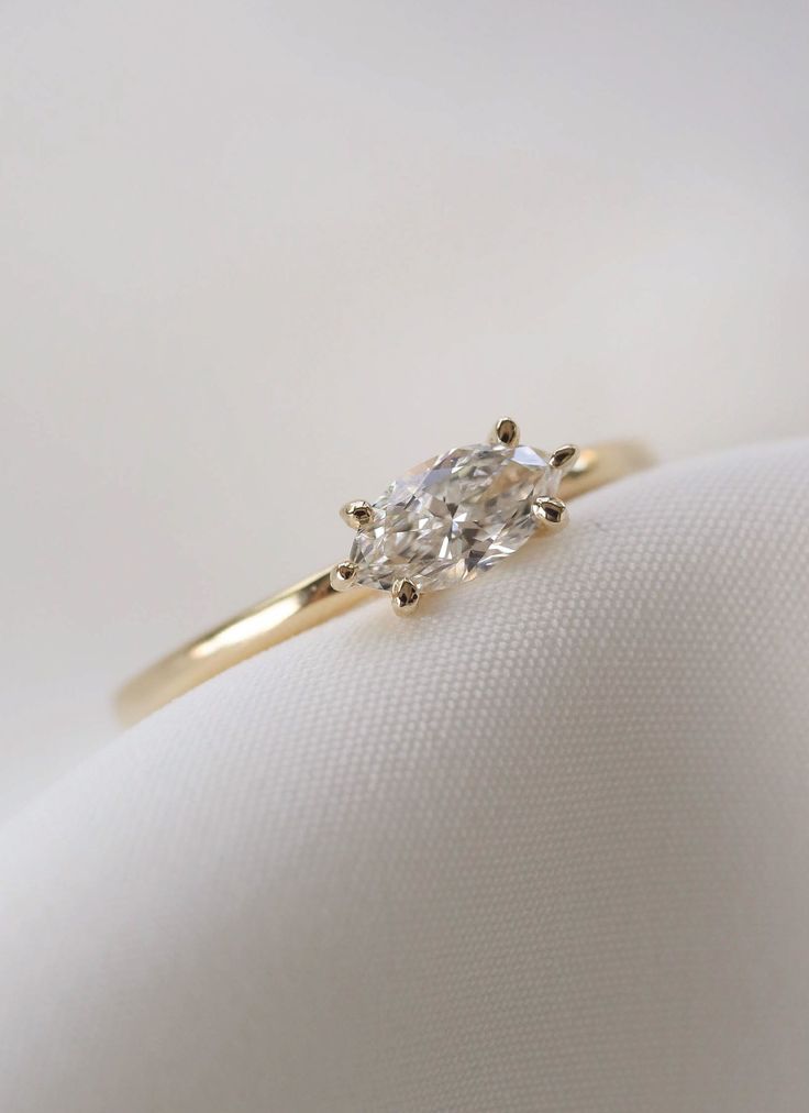 a yellow gold ring with an oval cut diamond in the center on a white cloth