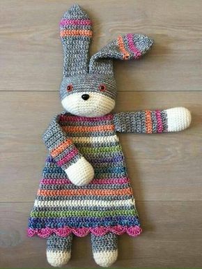 a crocheted stuffed animal wearing a colorful dress on top of a wooden floor