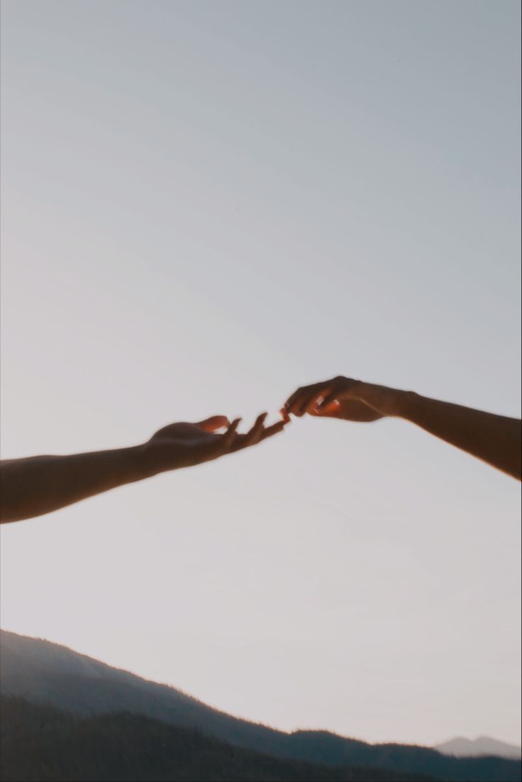 two people reaching out their hands to touch each other's fingers in the sky