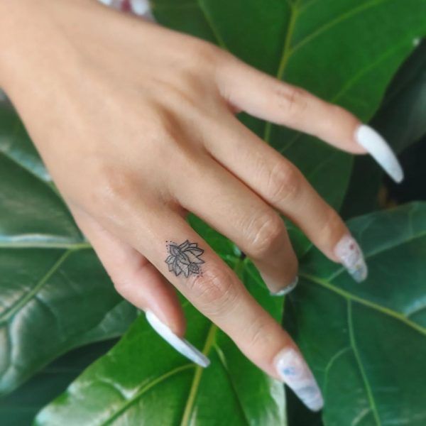 a woman's hand with a small flower tattoo on her left ring finger next to a green leaf