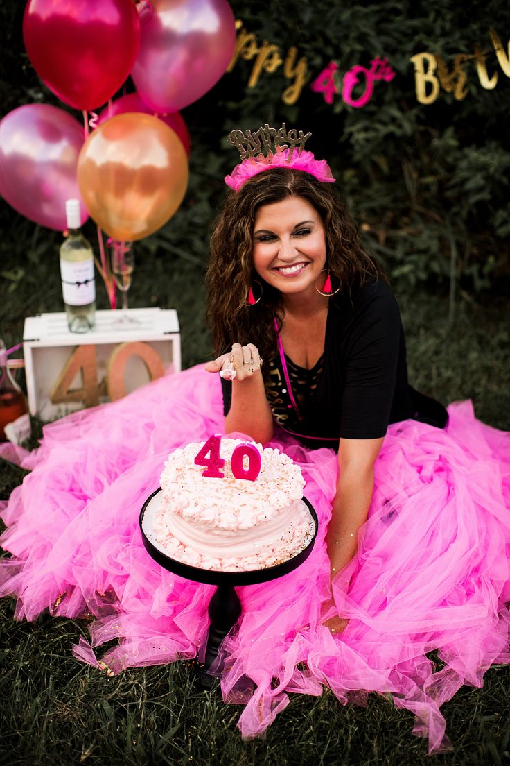 a woman sitting in front of a cake with the number forty on it and balloons behind her