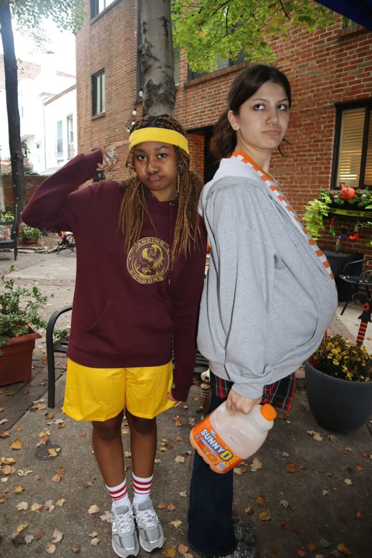 two young women standing next to each other in front of a tree and brick building