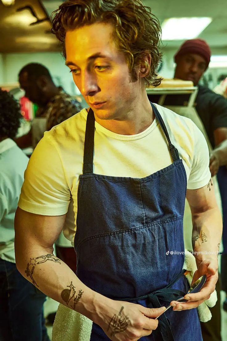 a man with tattoos on his arm and an apron holding something in his hand while standing next to other people