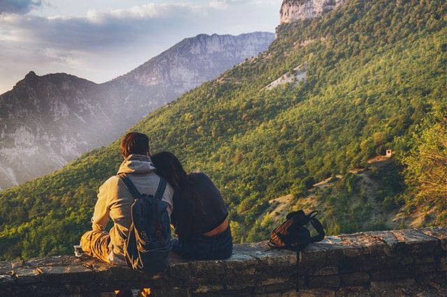 two people sitting on a wall looking at the mountains