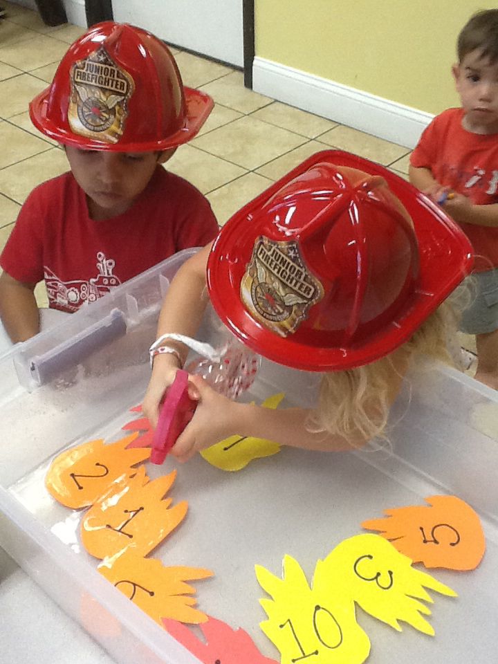 two children wearing fireman hats sitting at a table with cut outs in the shape of letters